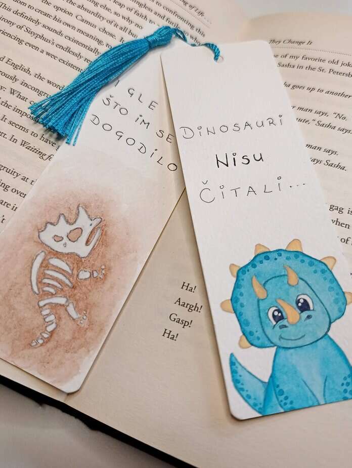 Ručno oslikani označivač stranica (bookmark) s motivom dinosaura Triceratopsom i tasselom, dimenzije 15x5, medij akvarel na 300 g/m² papiru. Idealno za ljubitelje knjiga.